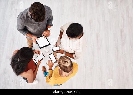 Exchanging data and information within an instant. High angle shot of a group of young designers using digital devices in synchronicity in an office. Stock Photo