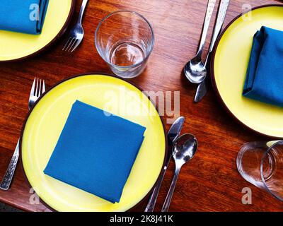 A place setting with blue napkins and yellow plates. Colorful Instagrammable hip restaurant table layout Stock Photo