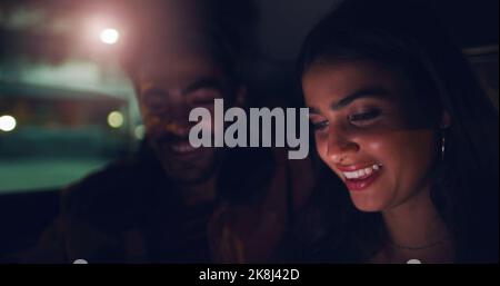 A night out is just what we need. a young couple looking at something on a screen while sitting in a car. Stock Photo