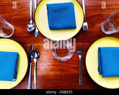 A place setting with blue napkins and yellow plates. Colorful Instagrammable hip restaurant table layout Stock Photo