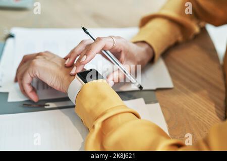 How effectively are you managing your time at work. Closeup shot of an unrecognisable businesswoman checking her wristwatch while writing notes in an Stock Photo