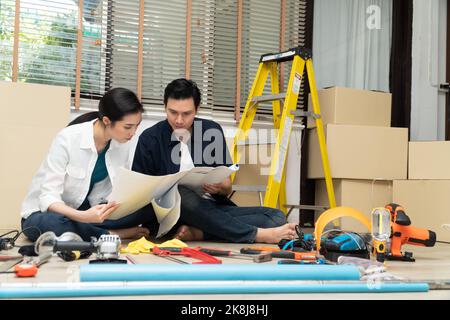 Happy Creative young Asian couple renovating house together and using a blueprint for renovation planning and how to   decorate and arrange the furnit Stock Photo