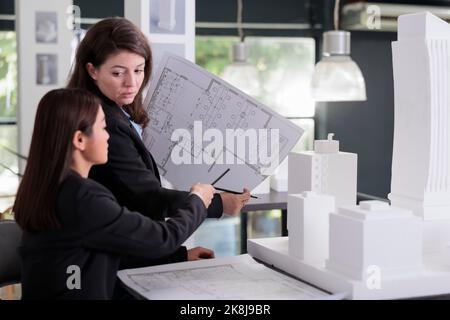 Architect and engineer holding blueprint, discussing construction project sketch, working with cad in coworking space. Employees in architecture office looking at cad together. Stock Photo
