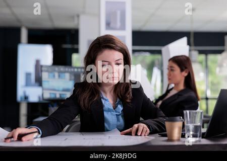 Architect working with project blueprint, cad designer in coworking space, architecture office employee at workplace desk. Real estate agency worker looking at engineering plan. Stock Photo