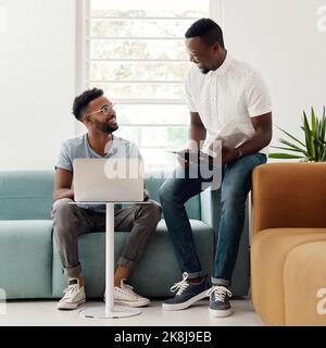 He is the office jokester. Full length shot of two handsome businessmen sitting together and reading paperwork while using a laptop in the office. Stock Photo