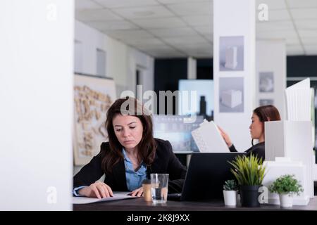 Cad designer working with project blueprint in coworking space, architecture office employee at workplace desk, medium shot. Real estate agency worker looking at technical plan. Stock Photo