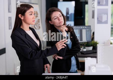 Thoughtful architects looking at 3d building printed model, discussing exterior design, working on construction project, teamwork. Architecture designers thinking, real estate workers cooperation Stock Photo