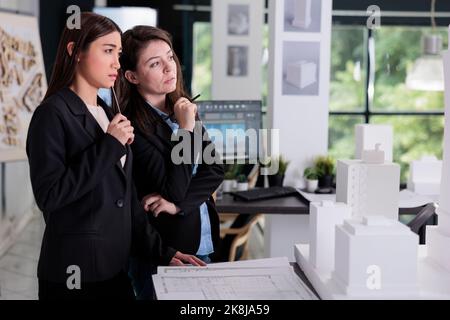 Thoughtful architects discussing 3d building printed model, working on construction design project. Architecture designers thinking, real estate workers cooperation in coworking space Stock Photo