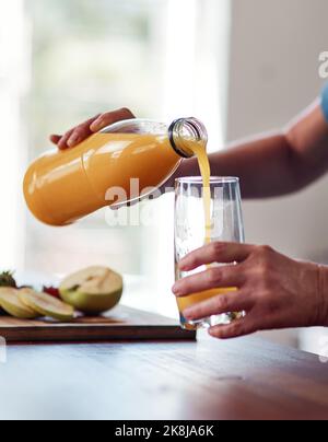 She loves her orange juice. an unrecognizable senior woman pouring herself a glass of orange juice while preparing breakfast in the kitchen. Stock Photo