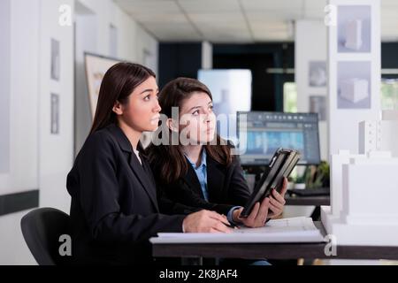 Architects working with tablet, looking at building printed model in coworking space, side view. Employees teamwork in architecture office, real estate agency project, 3d modeling Stock Photo