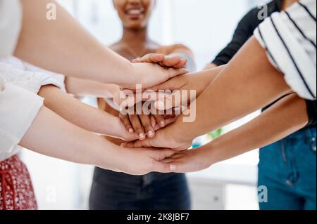 Success is a combined effort. a group of unrecognizable businesspeople joining hands together in a huddle inside an office. Stock Photo