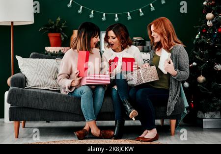 What did you get. three attractive middle aged women opening presents together while being seated on a sofa during Christmas time. Stock Photo