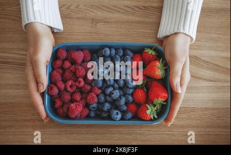 Fresh berries in woman hands. Various summer berries, strawberries, blueberries and raspberries in bowl on rustic wooden background Stock Photo