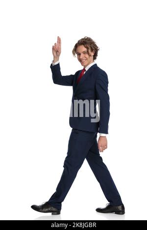 young man with curly long hair pointing fingers in the air and saluting, walking, smiling and posing in front of white background in studio, full body Stock Photo