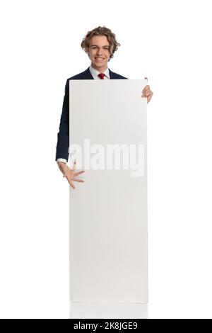 picture of happy blond businessman with long hair showing and recommending advertisement board in front of white background in studio Stock Photo