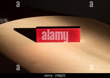 Poznan, Poland - 10.20.2022: Xiaomi Mi Bluetooth Speaker Portable red music speaker located on a wooden table in the rays of the sun Stock Photo