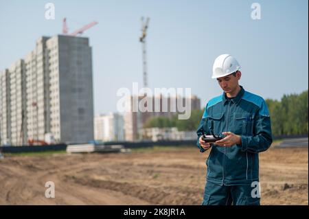 A man in a helmet and overalls controls a drone at a construction site. The builder carries out technical oversight. Stock Photo