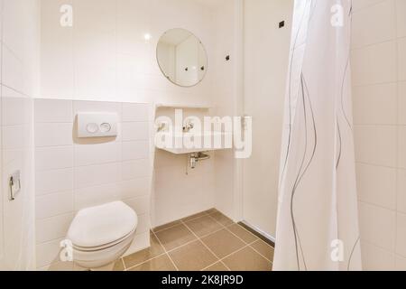 Bathroom with white tiled walls and open shower near sink and toilet in light Stock Photo