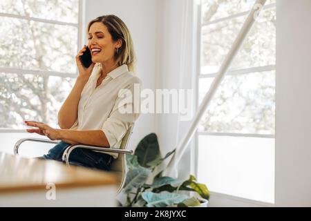 Happy young businesswoman taking a phone call in her home office. Successful businesswoman communicating with her business partners while working remo Stock Photo