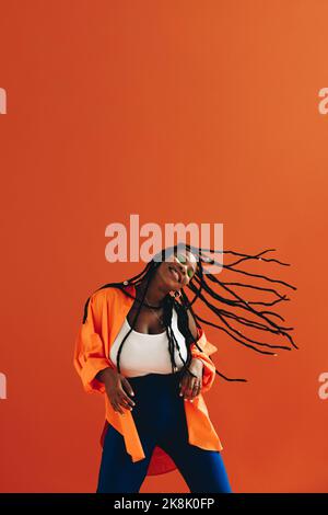 Happy young woman dancing and flipping her hair in a studio. Excited young woman celebrating and having fun against an orange background. Energetic yo Stock Photo