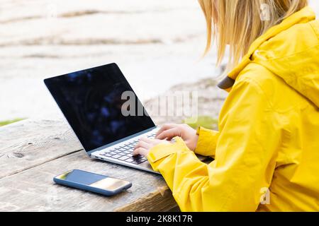 Remote worker relaxing near the lake and using a laptop. Working or studying over a laptop and smartphone. Stock Photo