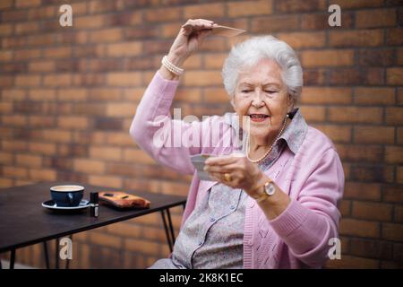 Happy senior woman combing her hair, enjoying coffee in city. Stock Photo