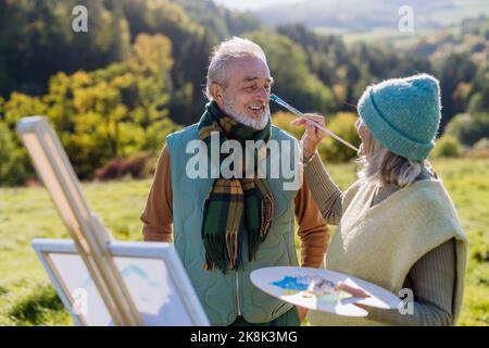 Senior couple painting together in nature, during autumn day. Stock Photo