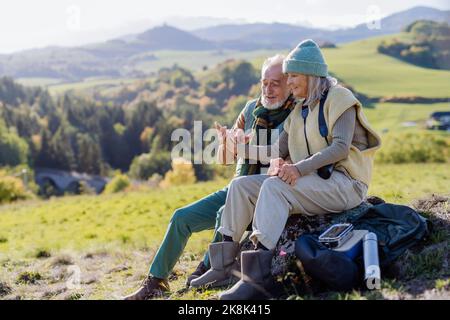 Senior couple having break, looking into phone during hiking in autumn nature. Stock Photo