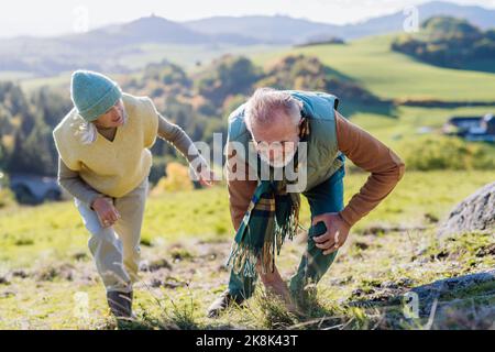 Senior man with having pain in knee during autumn walk, his wife taking care of him. Stock Photo