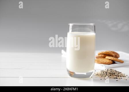 Vegan alternative food, sesame non-dairy milk with cookies on white wooden background, copy space. Homemade White Sesame milk on white background Stock Photo