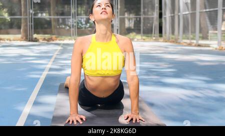 Beautiful Latin woman dressed in sports doing cobra pose outdoors. Healthcare with yoga therapy concept.  Stock Photo