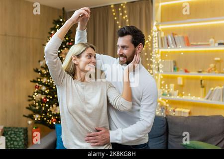 Christmas family couple, man and woman celebrating new year near tree at home, lovers dancing and having fun smiling and hugging.