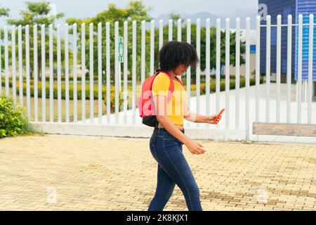 Afro woman walking and reading a text message on her cell phone Stock Photo