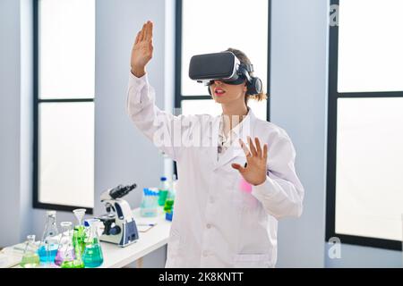 Young woman wearing scientist uniform using virtual reality goggles at laboratory Stock Photo