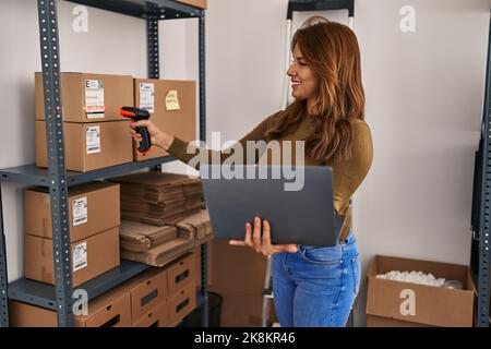Young latin woman business worker scanning package using barcode reader at office Stock Photo
