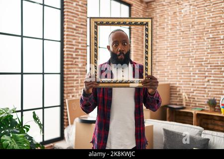 African american man putting face in empty frame making fish face with mouth and squinting eyes, crazy and comical. Stock Photo