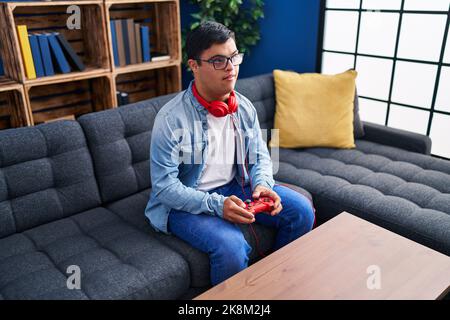 Down syndrome man playing video game sitting on sofa at home Stock Photo