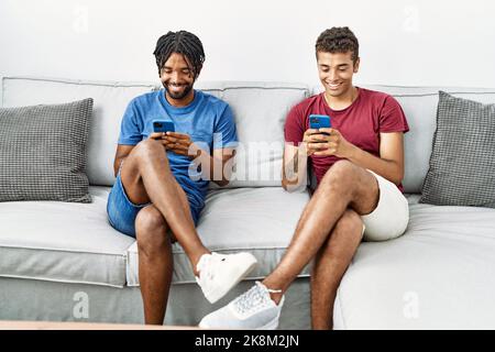 Two men friends using smartphone sitting on sofa at home Stock Photo