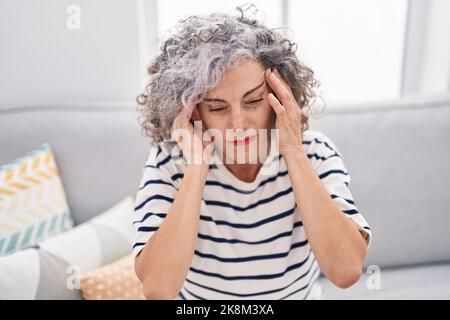 Middle age grey-haired woman suffering for headache sitting on sofa at home Stock Photo