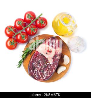 Fresh raw meat beef steak with bone with spices, rosemary, tomatoes, garlic and olive oil on wooden cutting board isolated on white background. Top vi Stock Photo