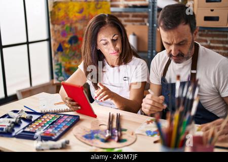 Middle age man and woman artists drawing on notebook using touchpad at art studio Stock Photo