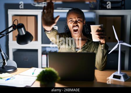 African woman working using computer laptop at night doing stop gesture with hands palms, angry and frustration expression Stock Photo