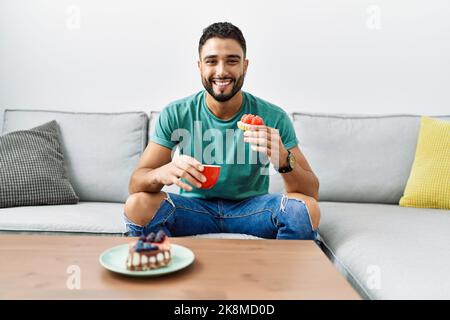 Young arab man having breakfast sitting on sofa at home Stock Photo