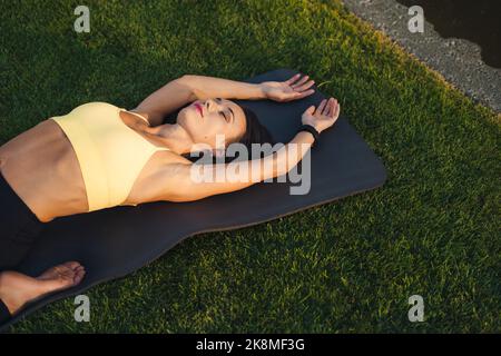 Beautiful young brunette woman stretching the muscles of her back, practicing on the green grassy lawn. Healthy active lifestyle. Body care. Training Stock Photo