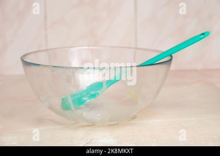 Dirty transparent glass bowl with silicone shovel. Dirty glass bowl after cooking. Dirty silicone shovel after home cooking. Stock Photo