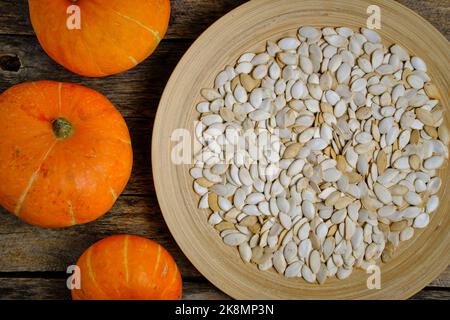 Pumpkins and pumpkin seeds in plate on wooden background Stock Photo