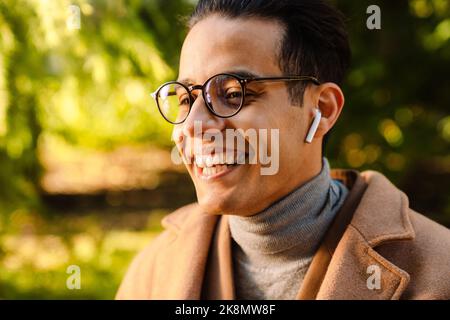 Young man wearing glasses listening music and laughing in park outdoors Stock Photo