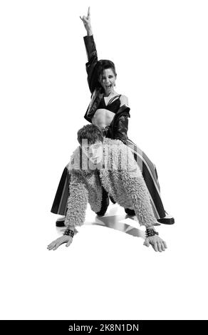 Portrait of expressive young woman in extravagant clothes sitting on back of young man. Black and white photography. Stock Photo