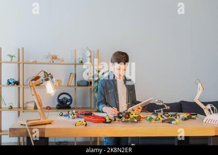 preteen boy holding digital tablet and writing in notebook near mechanical details of robotics model,stock image Stock Photo