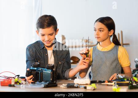 preteen girl holding screwdriver near friend looking at handmade car model at home,stock image Stock Photo